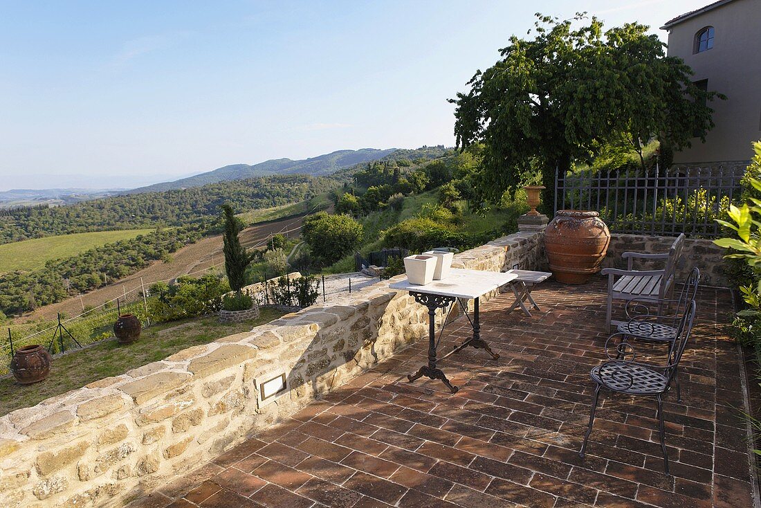 Terrasse mit Tisch und Stühlen auf Terrakottaboden und Blick auf mediterrane Landschaft