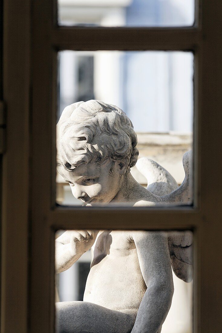 Blick durch Fenster auf Engelsfigur aus Stein