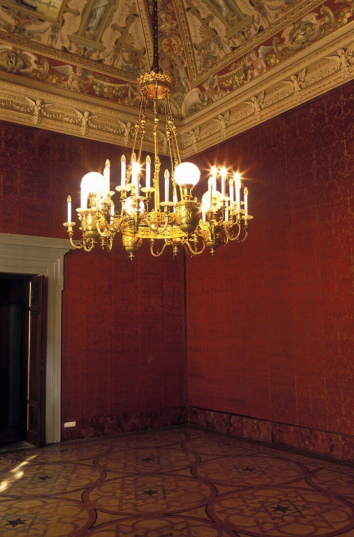 Brass chandeliers in a red anteroom with ceiling frescos and stucco