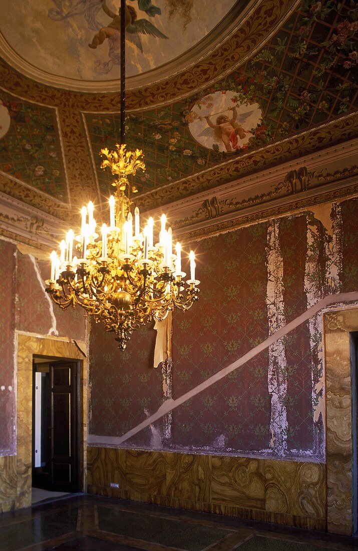 Unrestored anteroom of a castle with ceiling frescoes and a brass chandelier