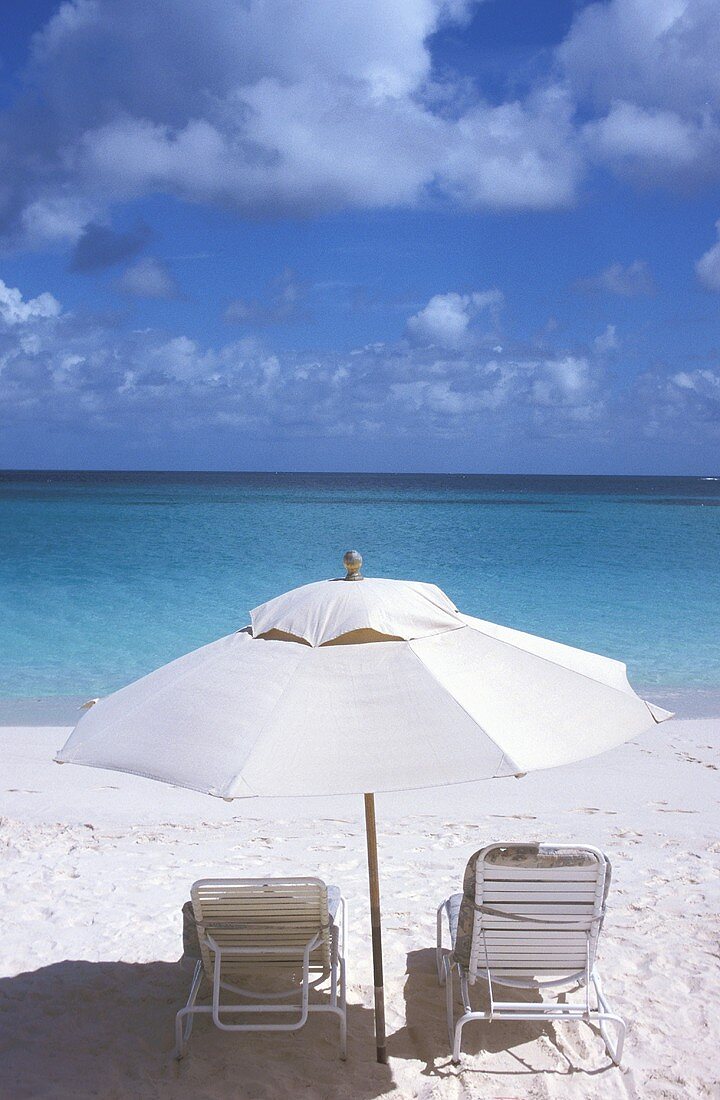 Weisser Sandstrand, Blick auf das Meer - Liegestühle stehen unter schattenspendendem Sonnenschirm