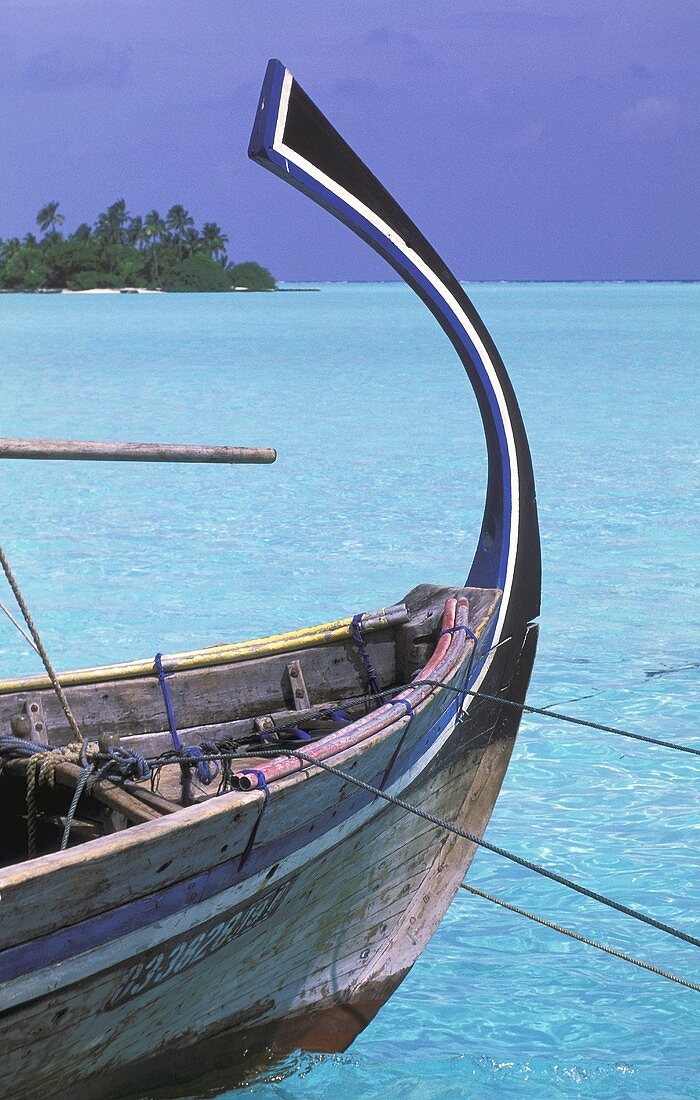 Holzboot mit geschwungenem Bootskiel schwimmt im türkisfarbenen Meer, im Hintergrund Blick auf eine Insel mit einem Palmenwald