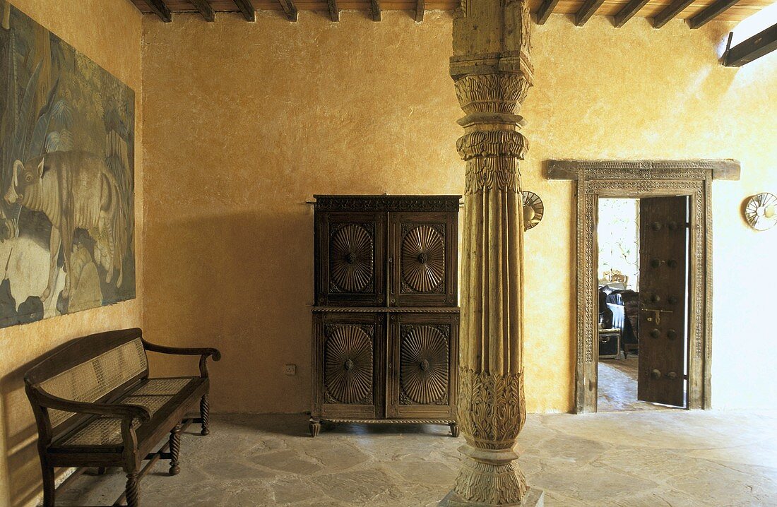 Wenig möblierter Raum mit gelber Wand und geschnitzter Holzstütze im afrikanischen Haus