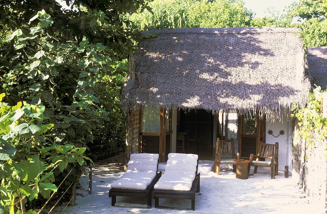 House on the Maldives -- in the courtyard two lounge chairs with white cushion covers stand in front of a palm hut
