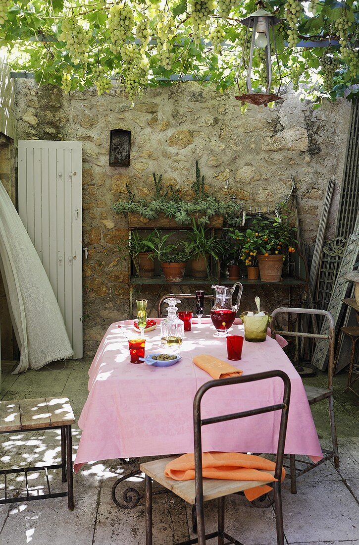 Erfrischungsgetränke auf Tisch mit rosa Tischtuch und Blumenstellage vor hoher Steinmauer
