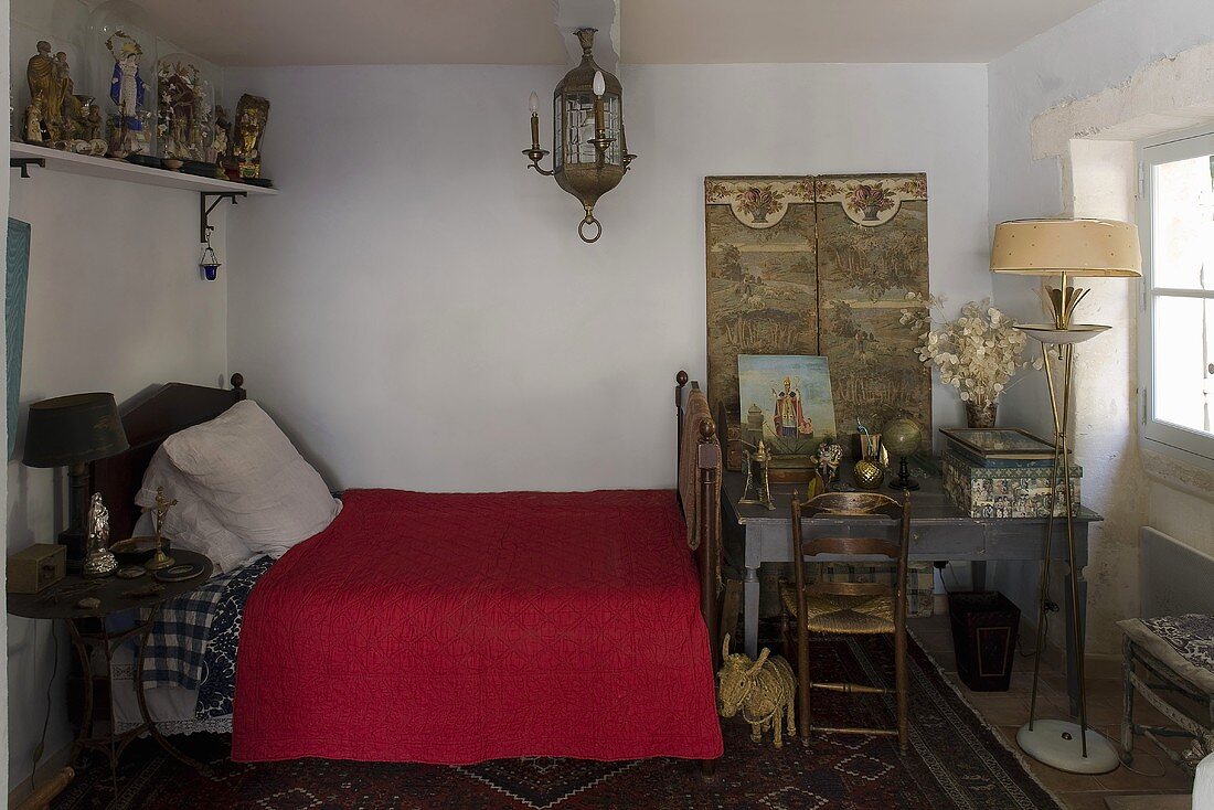 Schlafraum im Nordafrikastil mit roter Tagesdecke auf Bett und Tisch mit Stehlampe am Bettende