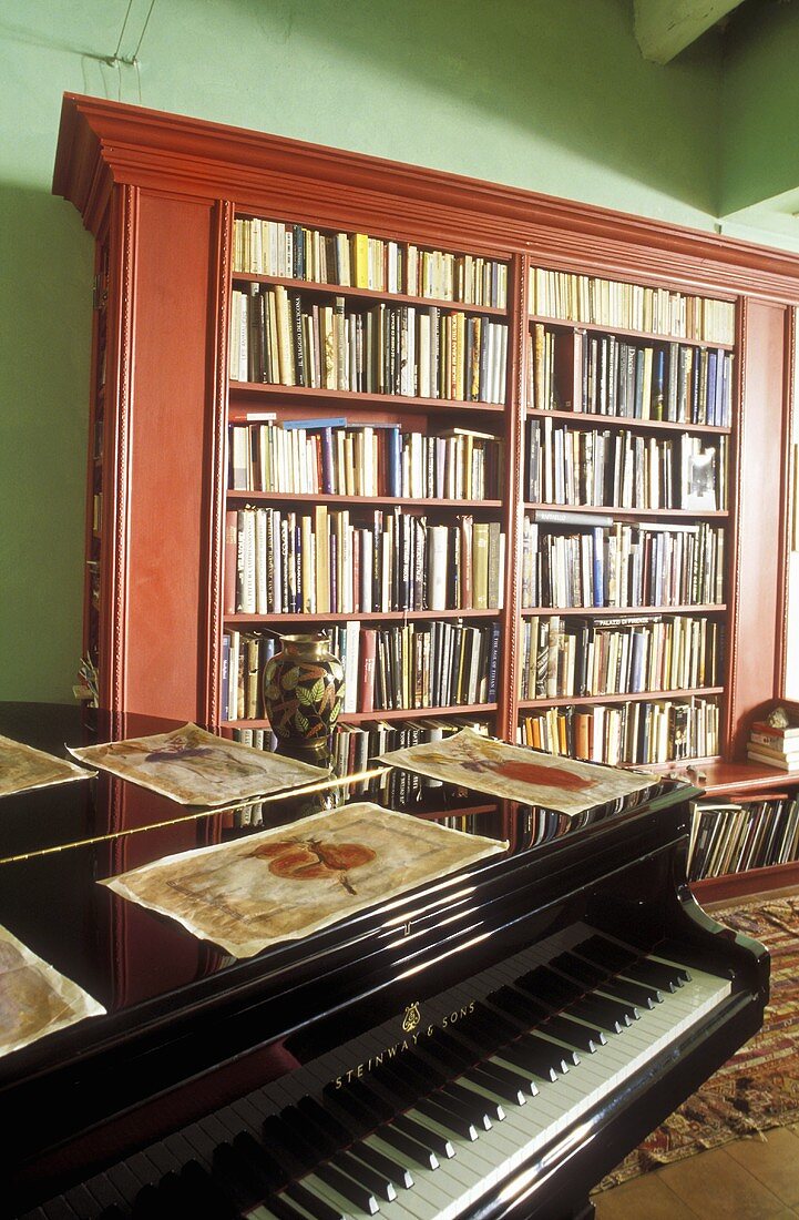 Wohnraum mit Klavier und Bücherschrank aus Mahagoni vor grüner Wand