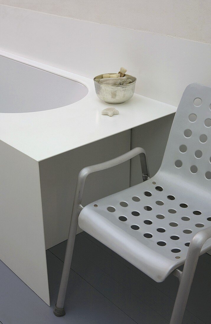 Grauer Metallstuhl mit gelochter Sitz- und Rückenfläche neben der Badewanne