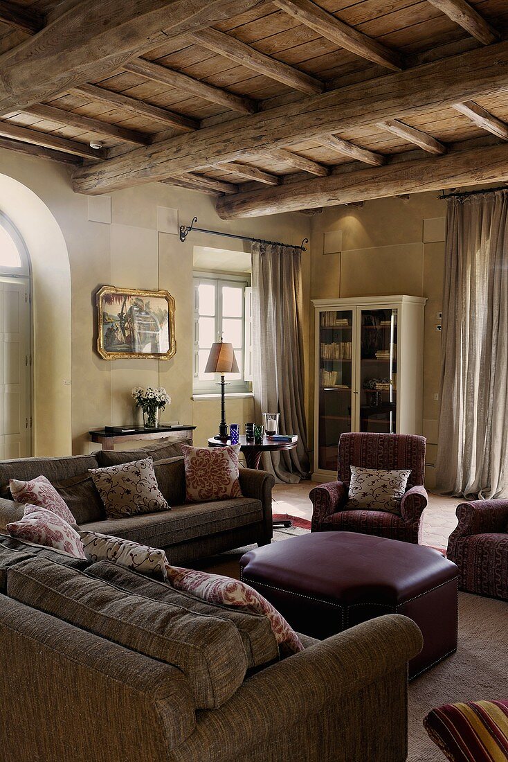 Wohnraum im Landhaus mit rustikaler Holzdecke über gemütlicher Sitzecke und Lederhocker