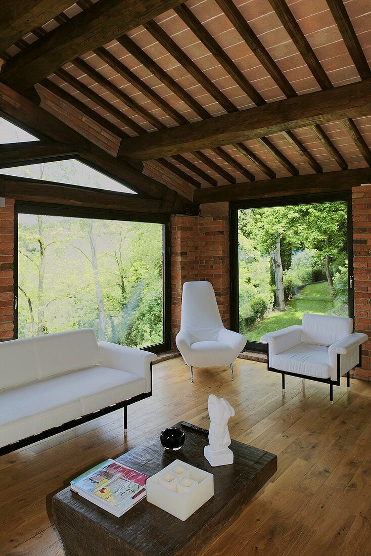 Renoviertes Landhaus mit Holzbalkendecke und hellen Sitzmöbeln vor raumhohen Fenstern