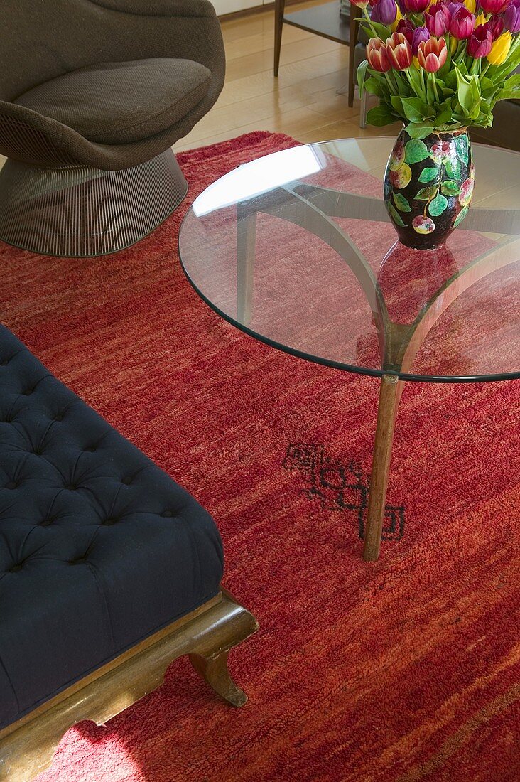 Glastisch mit buntem Tulpenstrauss auf rotem Teppich