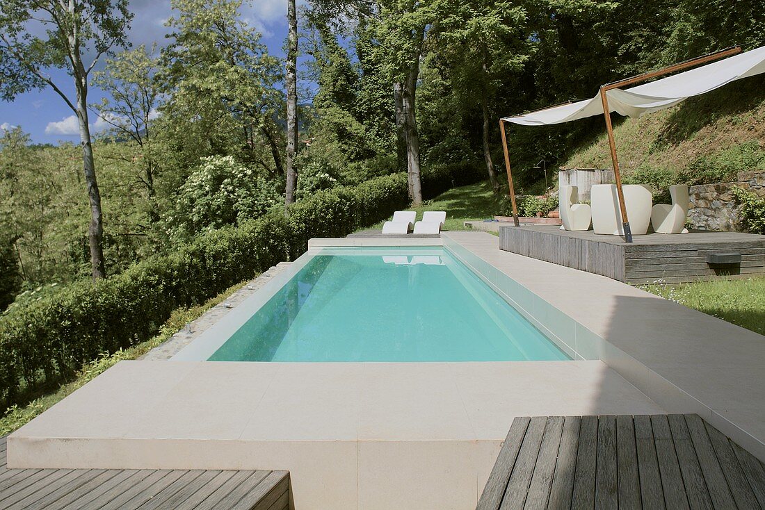 Türkisfarbener Pool mit Steineinfassung im Garten und überdachtes Holzdeck mit Outdoormöbeln