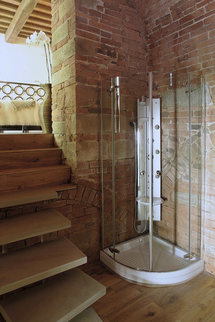 Duschkabine aus Glas in Zimmerecke aus Ziegelwänden und Holztreppe