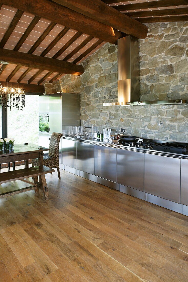 Edelstahlküche vor Natursteinwand und Holzbalkendecke im renovierten Landhaus
