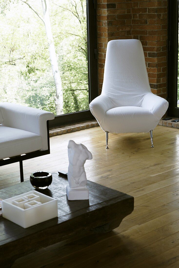 White armchair in the corner of a living room in front of floor to ceiling windows on a wooden floor