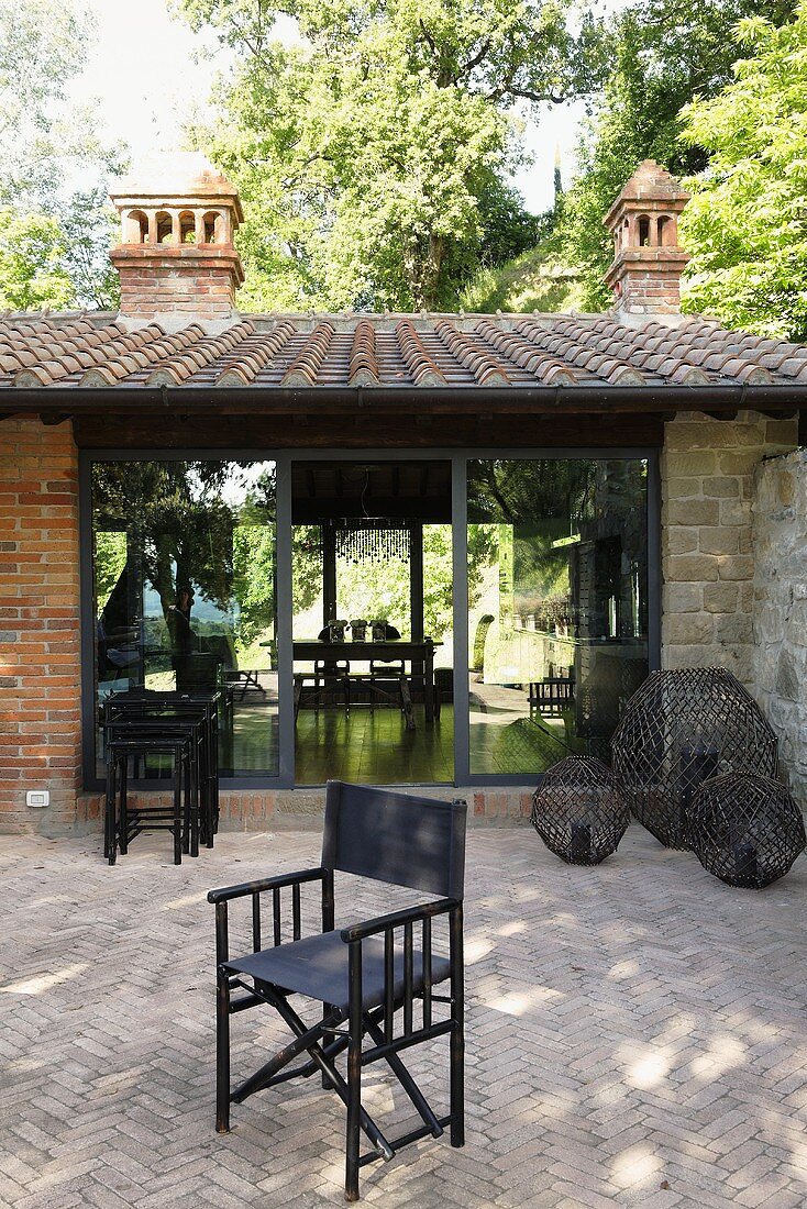 Chair on a stone terrace with a herringbone pattern in front of a Mediterranean country home with terrace windows