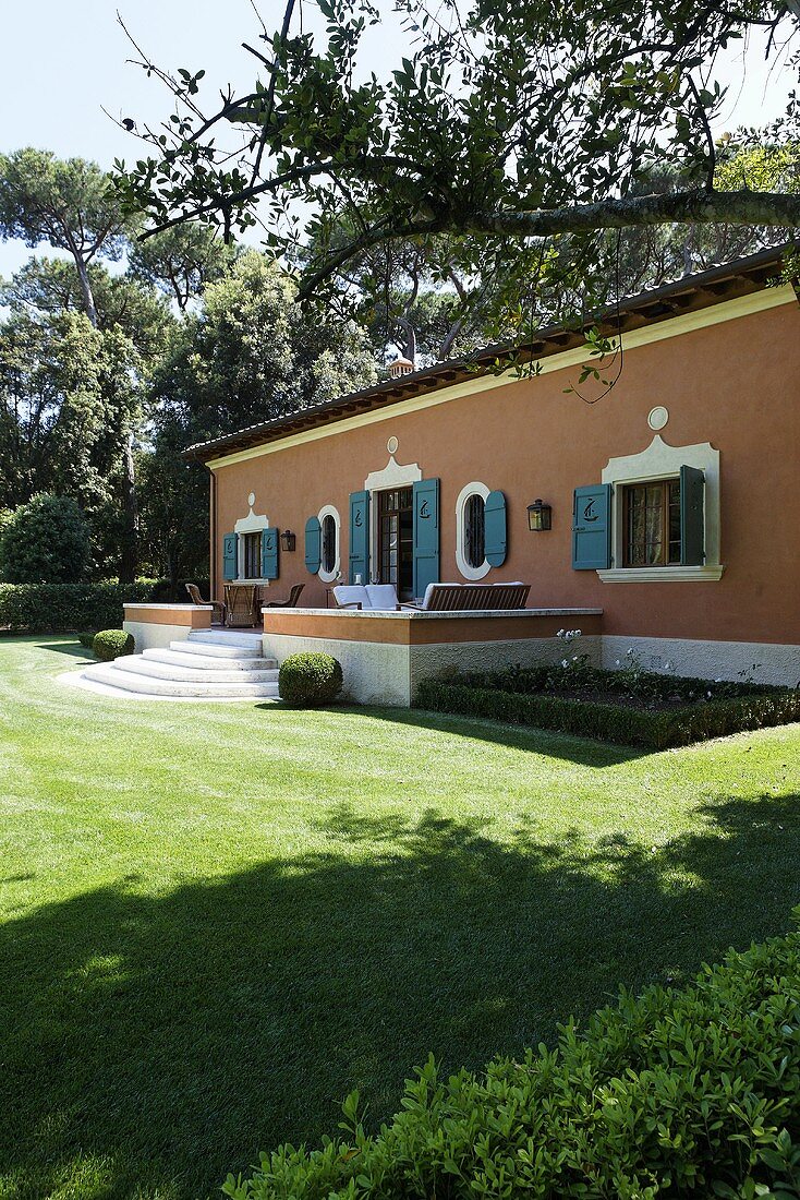 Mediterraner Villa mit ziegelroter Fassade und Terrasse in gepflegtem Garten