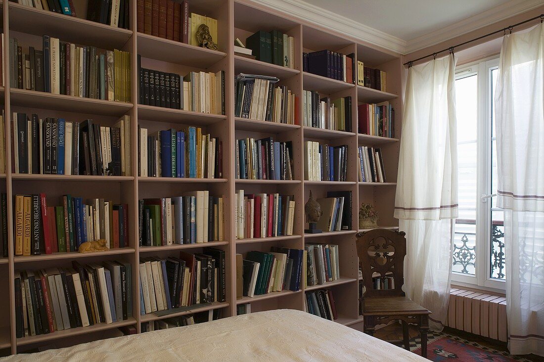 Rosafarbenes Bücherregal im Schlafraum und leichte Vorhänge am Fenster