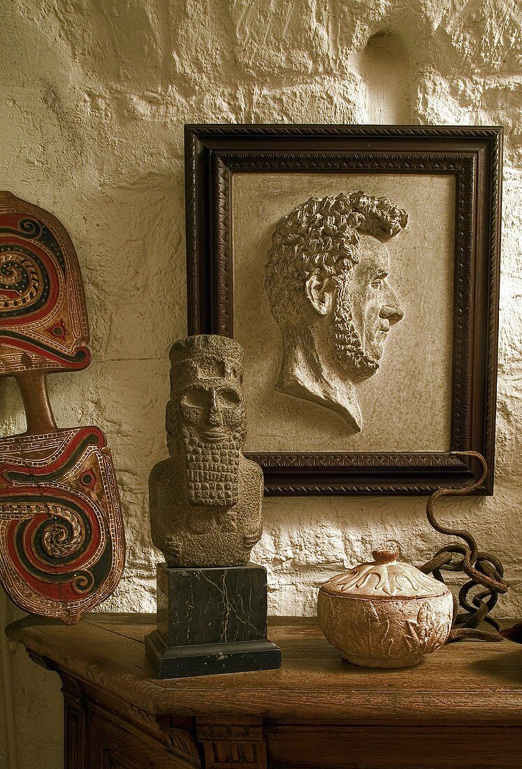 Framed half relief on a rustic stone wall and stone busts on a wooden table top
