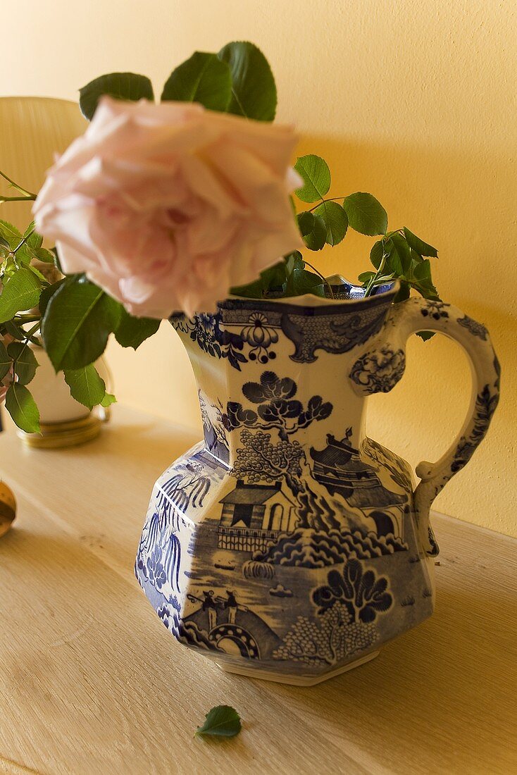 Blühende Rose in bemalter Porzellanvase auf Holzablage