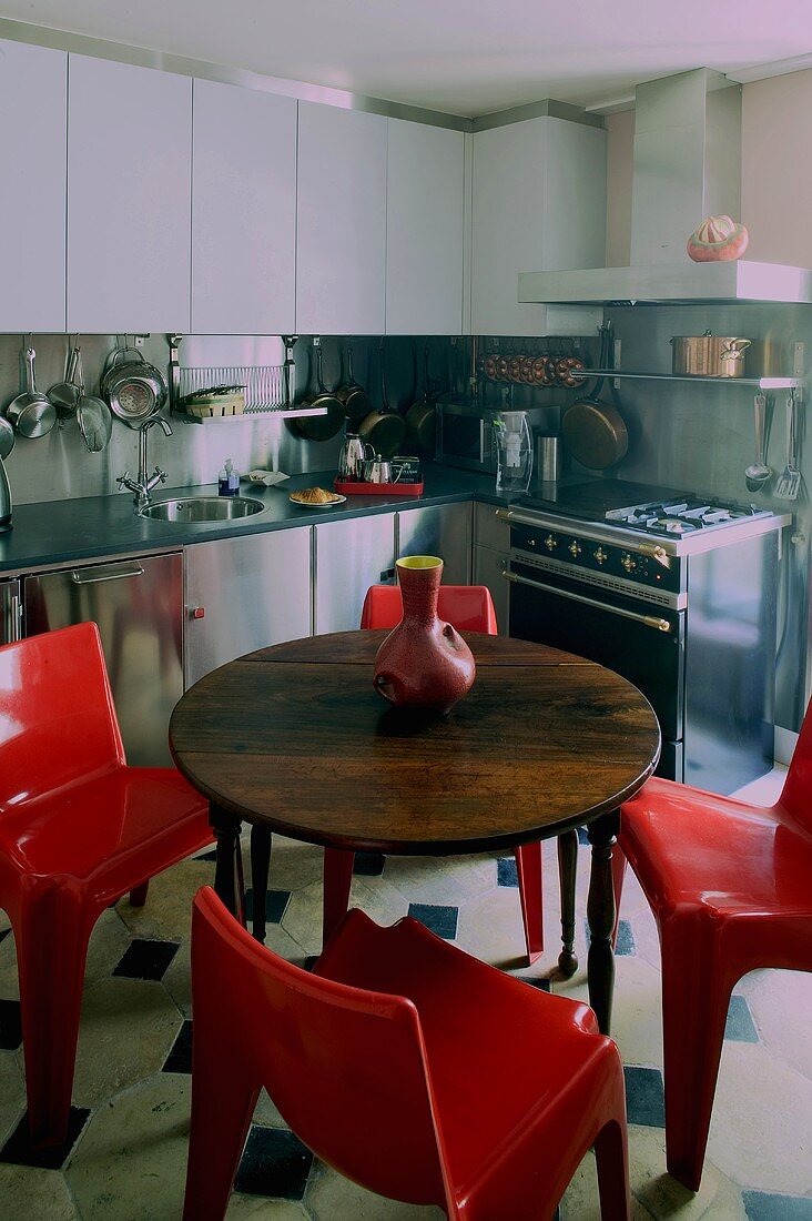 Round wooden table with red plastic chairs in a built-in kitchen