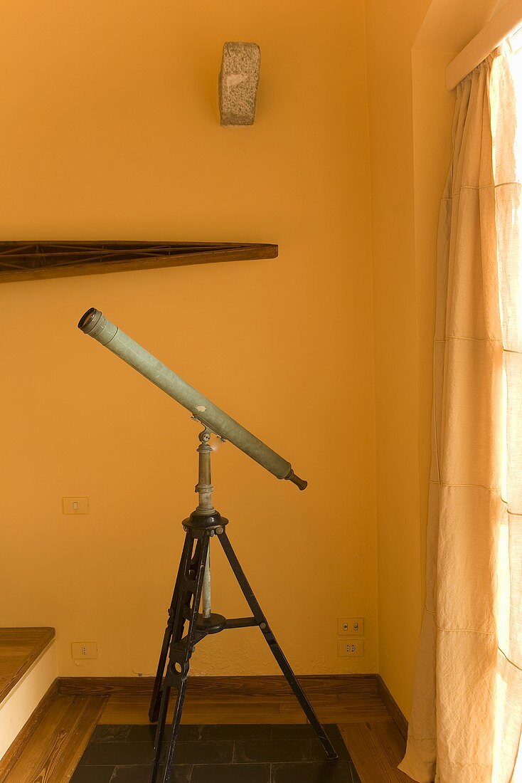 Antique telescope in front of a yellow wall