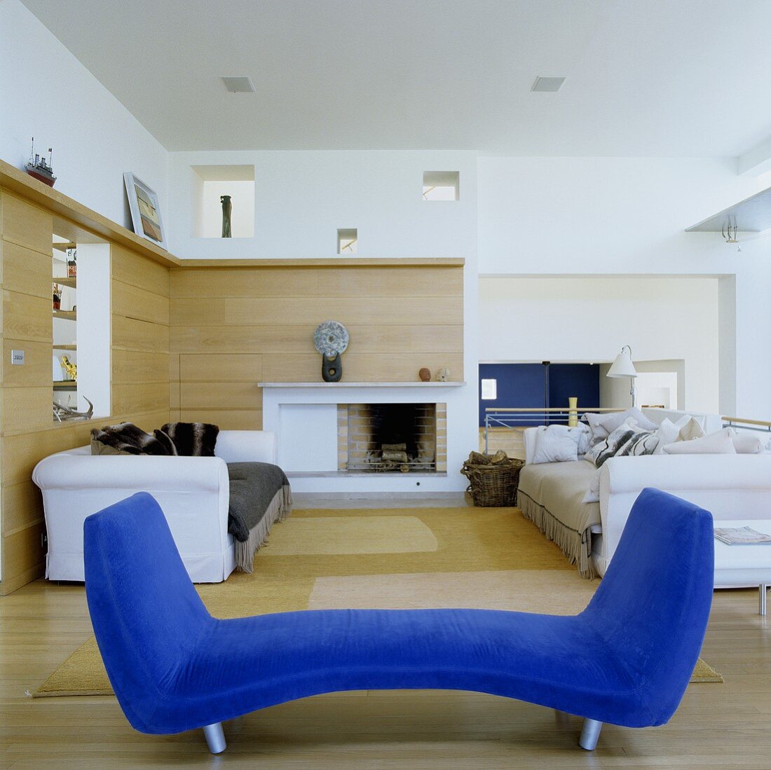 Blauer Diwan und weiße Sofagarnitur im offenen Wohnraum mit holzvertäfelter Wand und Kamin