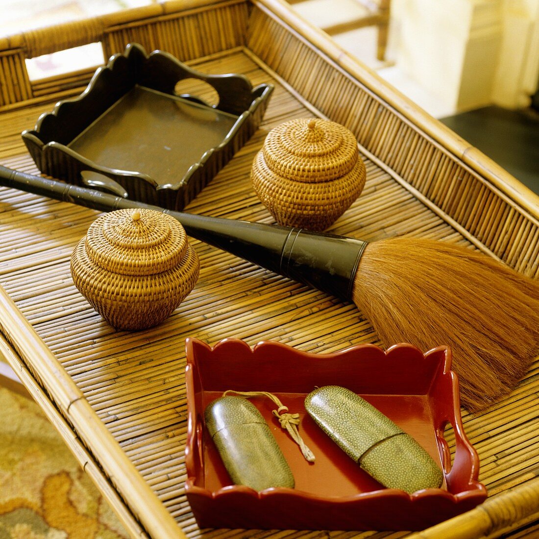 Stillleben auf einem Bambustablett mit lackierten Holzschalen, Minikorbgefässen und einem bauschigen Pinsel