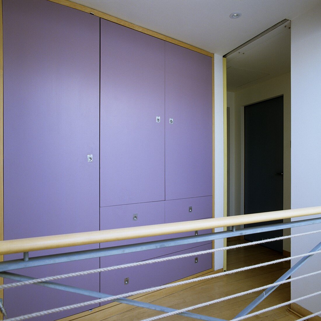 Einbauschrank mit violetten Türfronten auf Galerie und Treppenreling mit gespannten Seilen