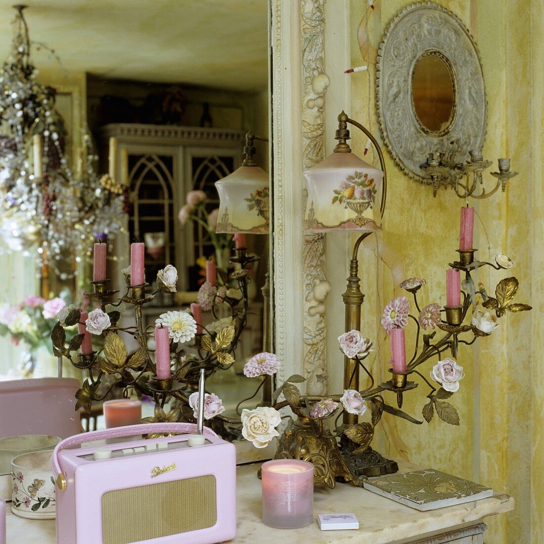 Vergoldeter Kerzenleuchter, antike Tischlampe und rosa Kofferradio vor Wandspiegel