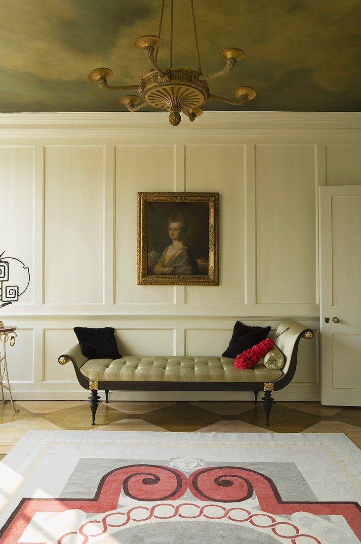 Elegante Chaiselongue vor weiss vertäfelter Holzwand mit Bild und Deckengemälde im Altbau - Wohnraum