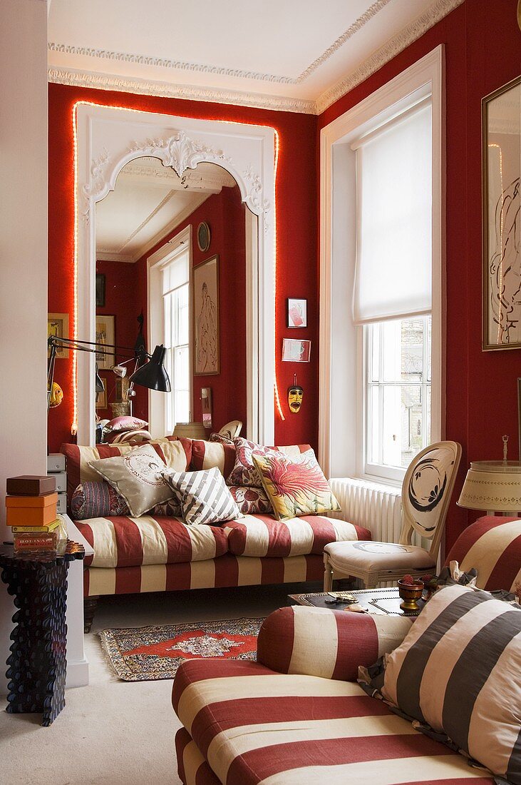 A living room in a villa with a red and white striped two-seater sofa in front of a floor-to-ceiling mirror with a chain of lights around a doorway in a red wall
