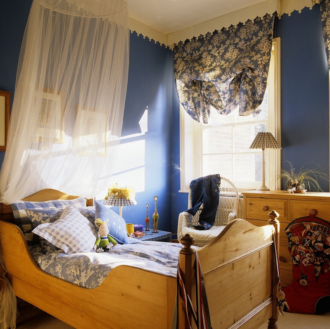 Kinderzimmer mit Holzbett und Baldachin und Lichtspiele auf blauer Wand