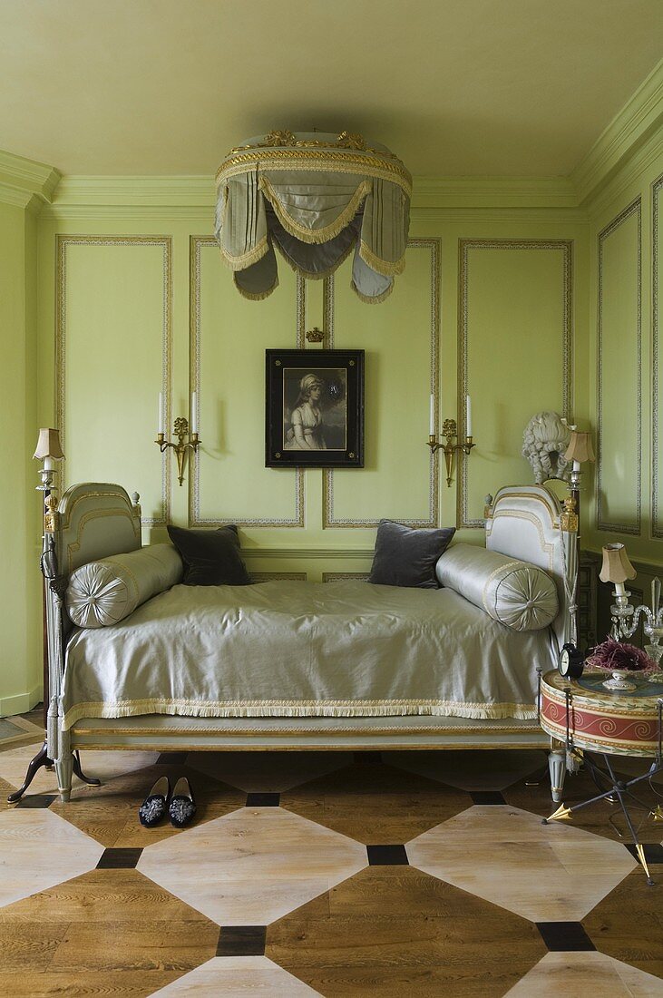 An elegant antique bed in front of a green wood panelled wall in a room with a painted wooden floor