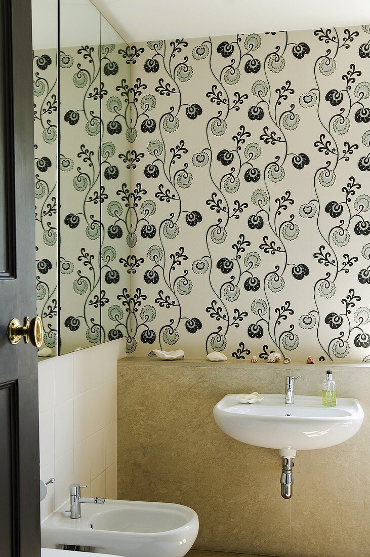 A bidet and a wash basin in a mini bathroom and black and white patterned wallpaper