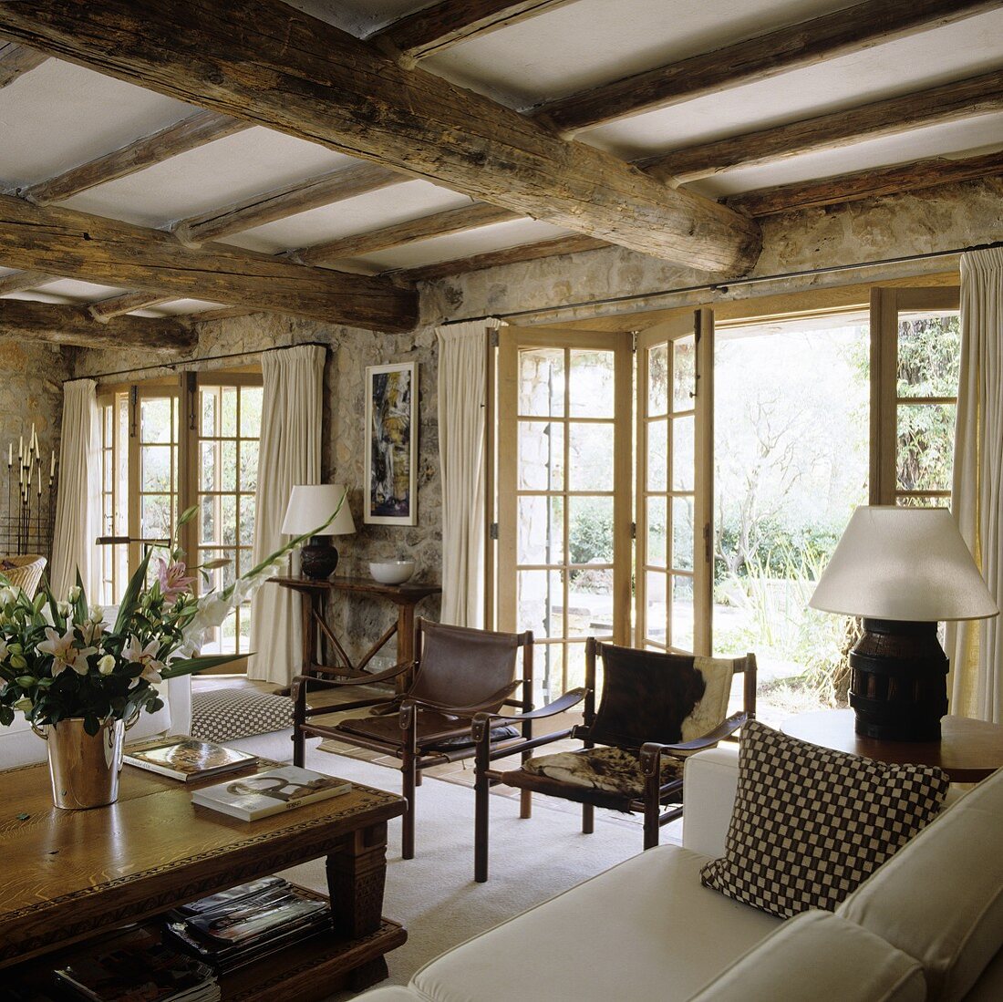 Elegantes Landhaus mit rustikaler Holzbalkendecke und Lederstühle vor offener Terrassenfalttür