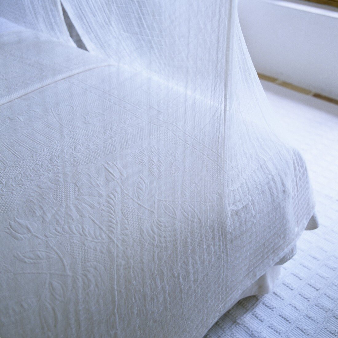 The corner of a bed with white airy fabric