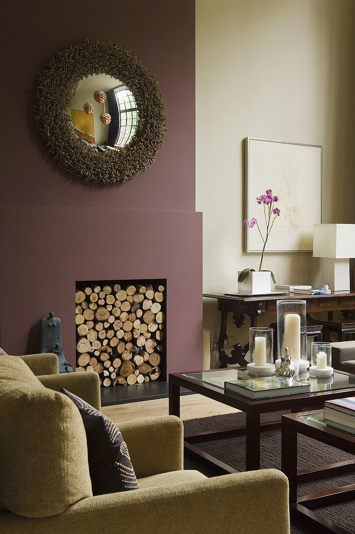 Glass-topped occasional tables with dark wood frames in front of a dark red chimney breast with a fireplace filled with wood
