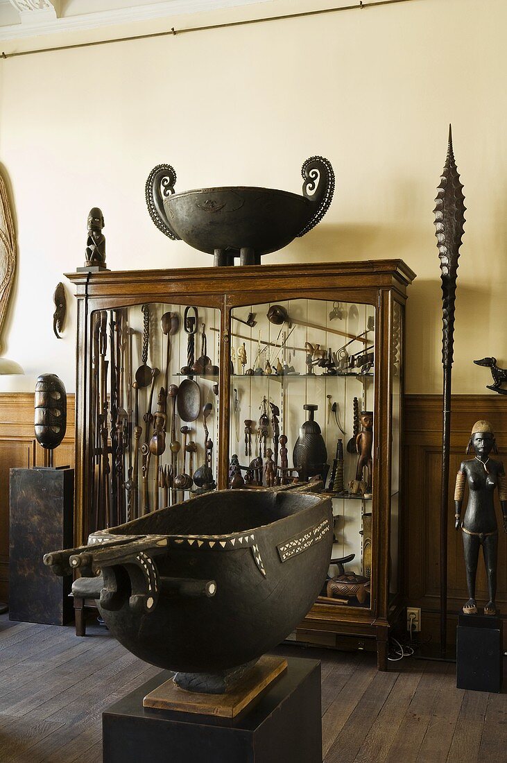 A metal container on a pedestal and a cabinet containing a collection of African handicrafts