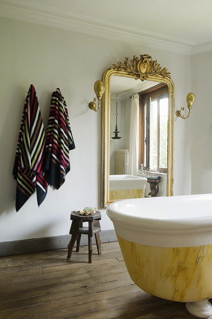A bathroom in a country house with a free-standing antique bathtub and a wall mirror with a golden frame