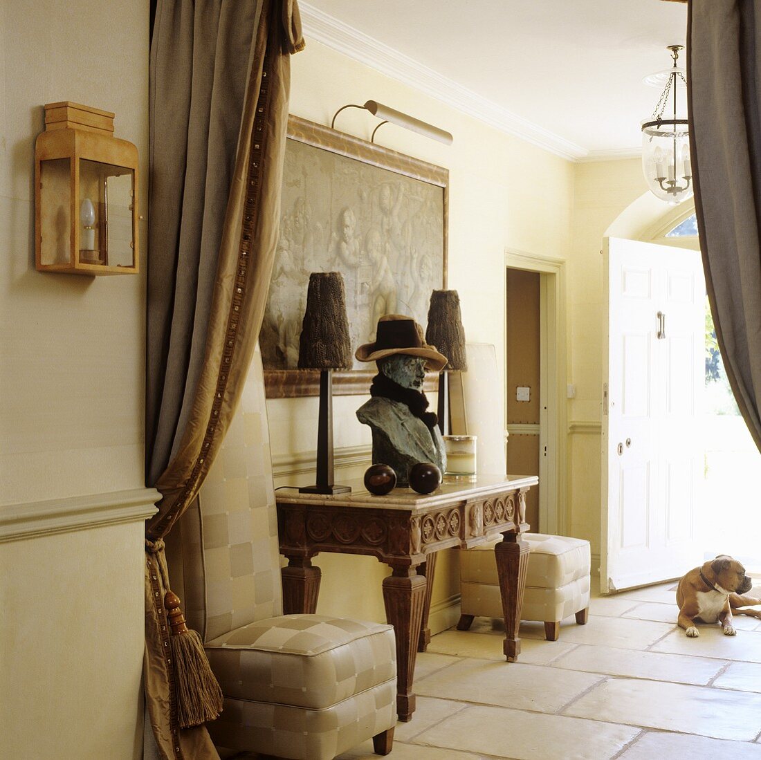 Blick durch offenen Vorhang in ländlichen Hausflur auf holzgeschnitztem Tisch mit Büste und Tischlampen