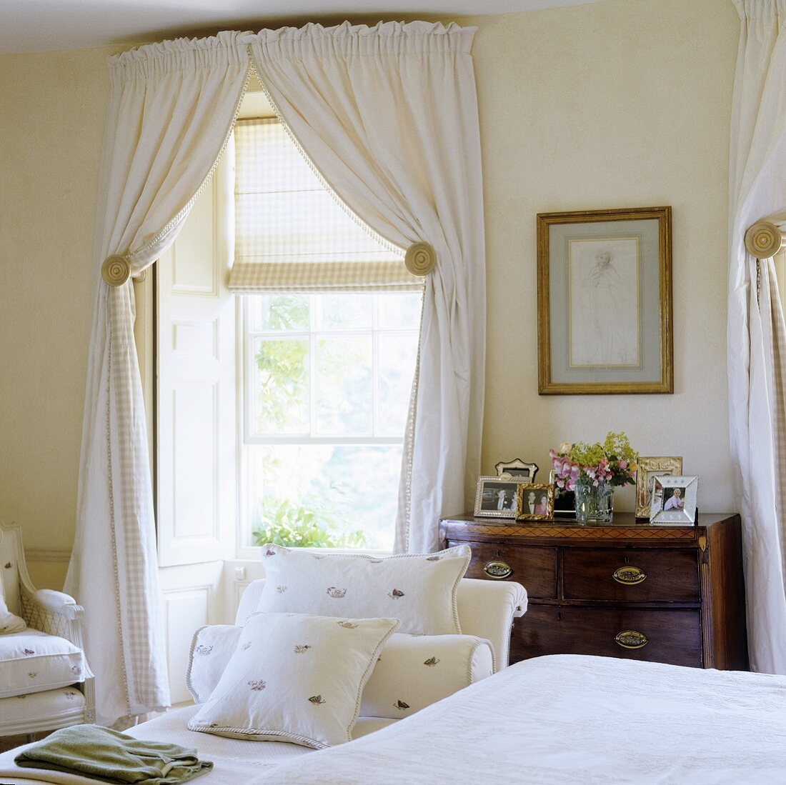 An elegant, country-house style bedroom with a white curtains and a blind at the window
