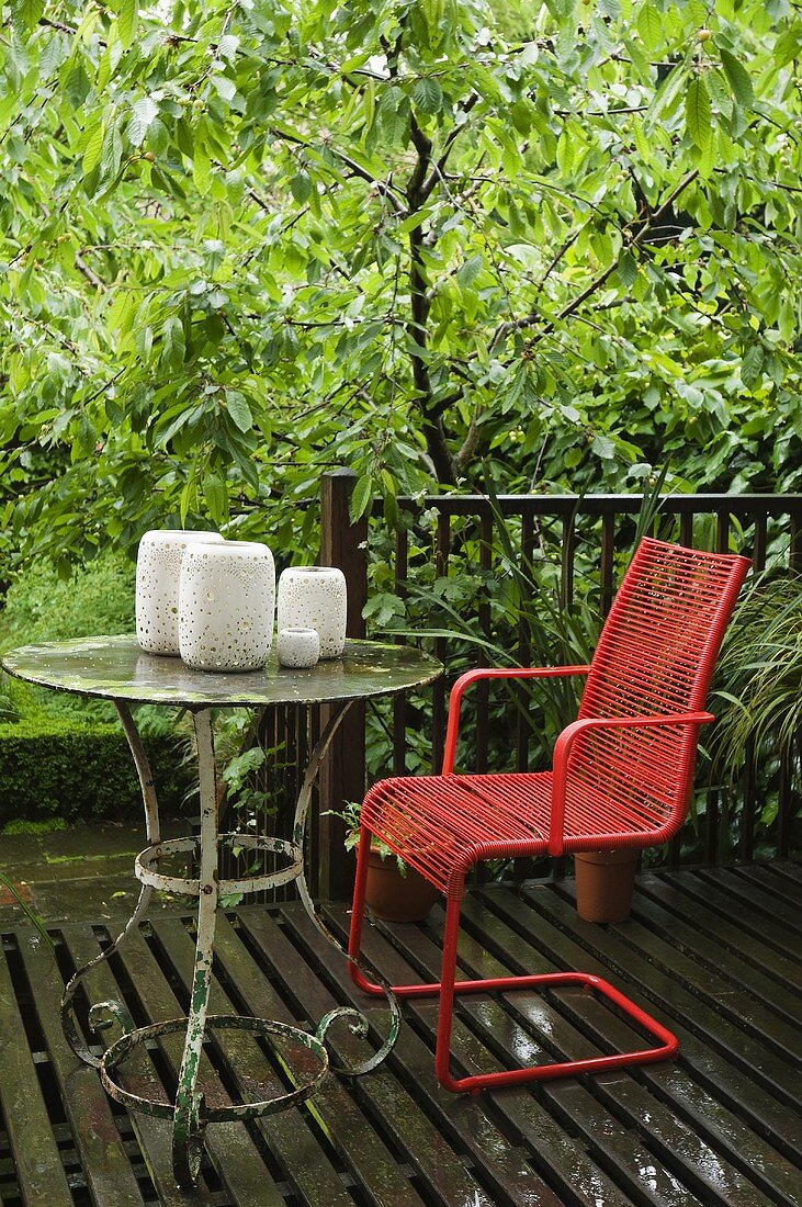 Roter Gartenstuhl und Vintage Metalltisch mit Windlichterset auf Holzterrasse