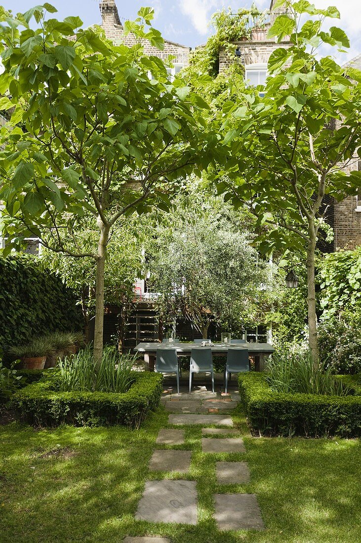 Sonniger Tag im Garten mit Hecke um Baum und idyllischer Terrassenplatz