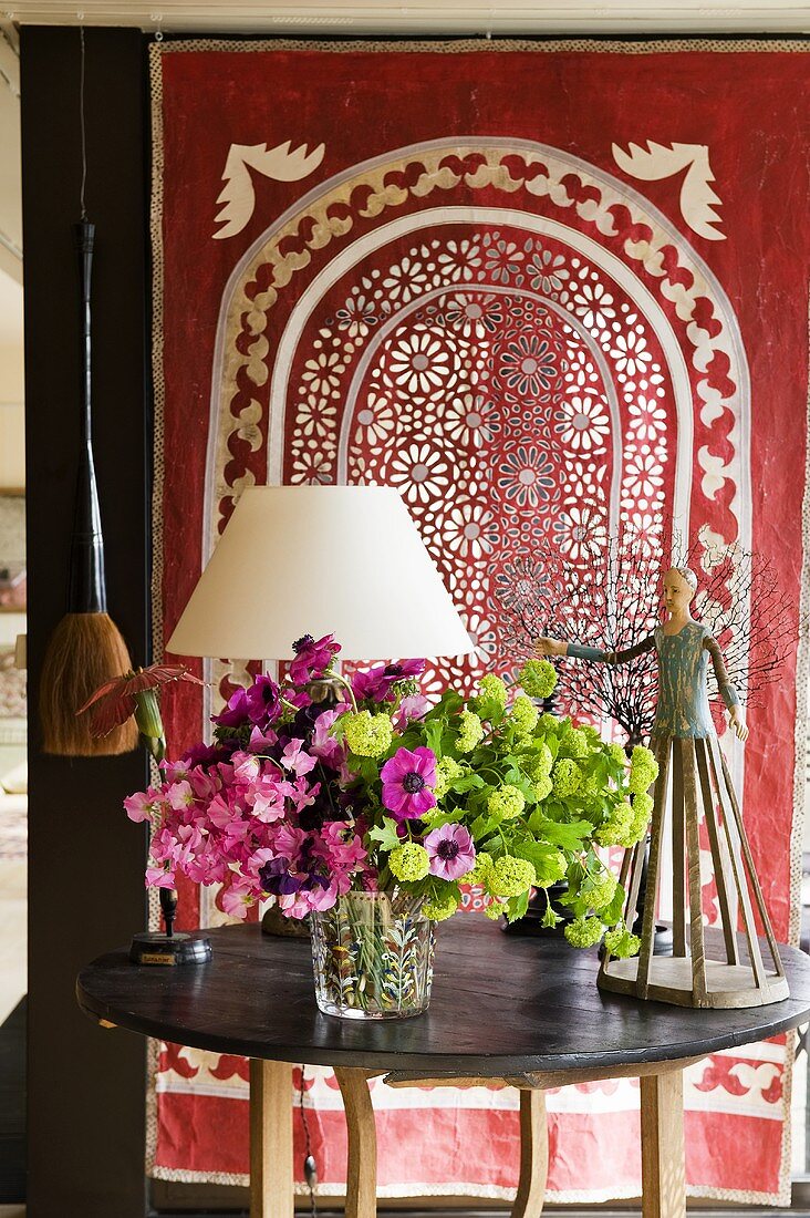 Blumen auf Holztisch vor rotem Tuch mit Lochmuster im folkloristischen Stil