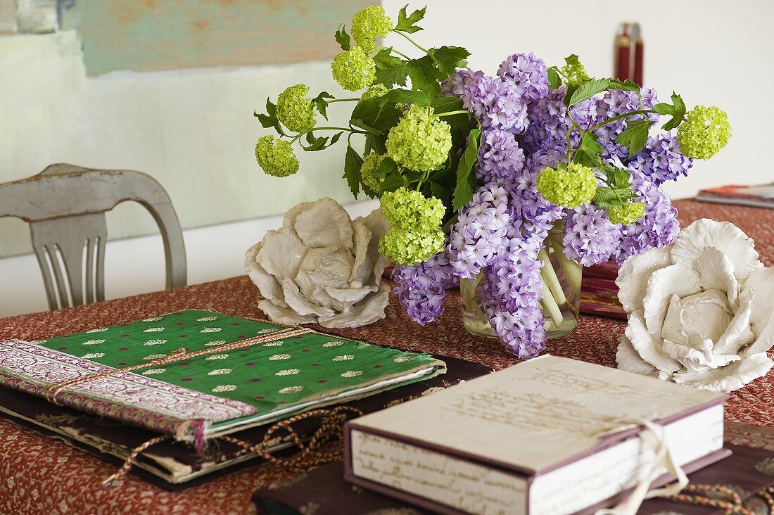 Fliederstrauss und bunte Mappen auf Tisch mit gemusterter Tischdecke
