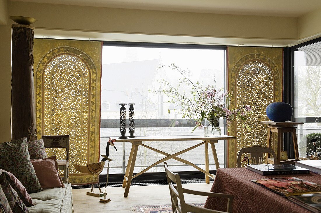 An ethnically designed living room with a light wooden table and a ethnic cloths in front of a window