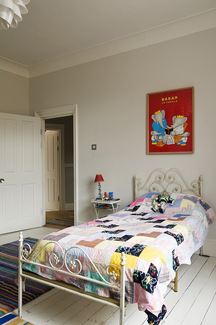 A patchwork quilt on an antique, white metal bed standing on white-painted floor-boards in a child's bedroom