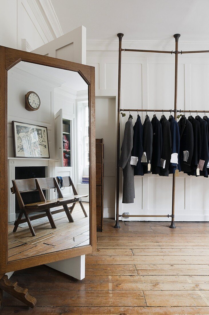 weiße Holzvertäfelung im Wohnzimmer - Atelier mit Schneiderspiegel mit Spiegeleffekten und eingespannter Kleiderstange mit gehängten Jacken