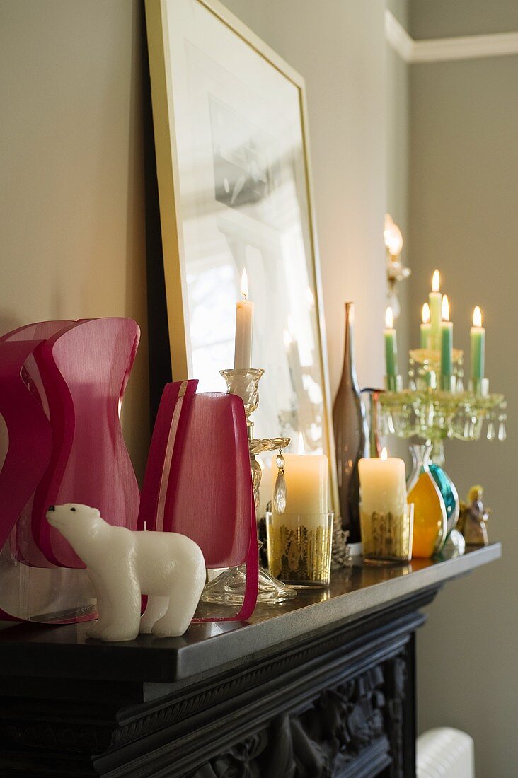 Pinkfarbene Vasen und brennende Kerzen auf schwarzem Kaminsims